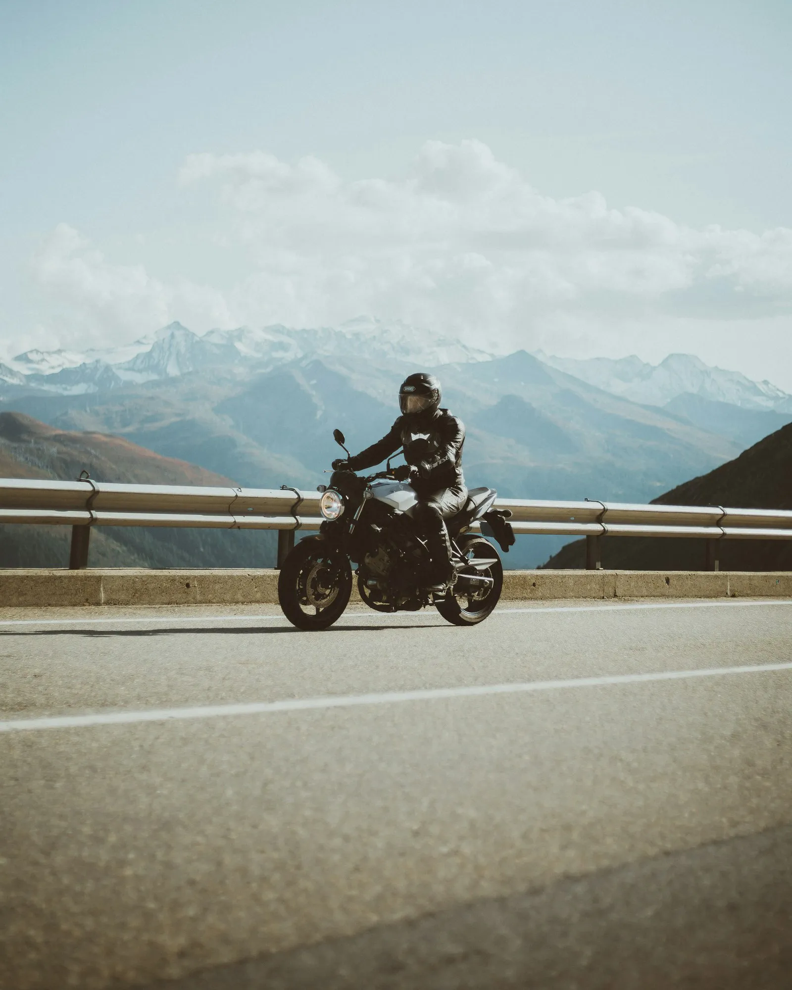 A motorcyclist riding along an Alpine road with snowy peaks behind