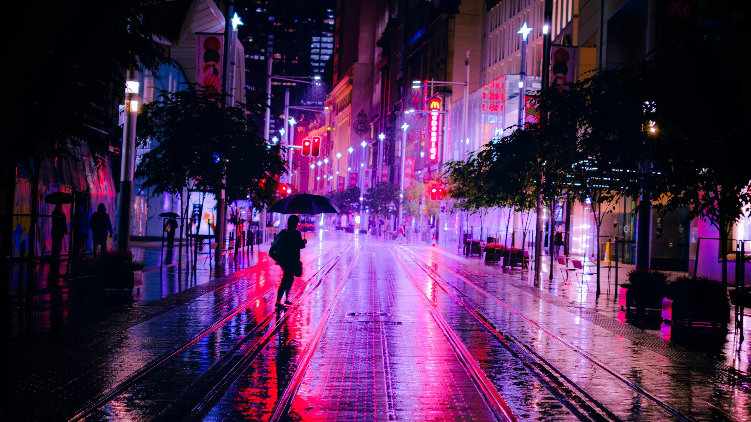 A rainy city street at night, lit in pink and purple neon