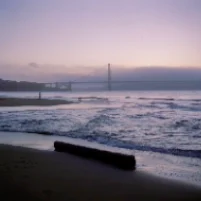 A copied photo of a beach at dawn, a bridge in the distance